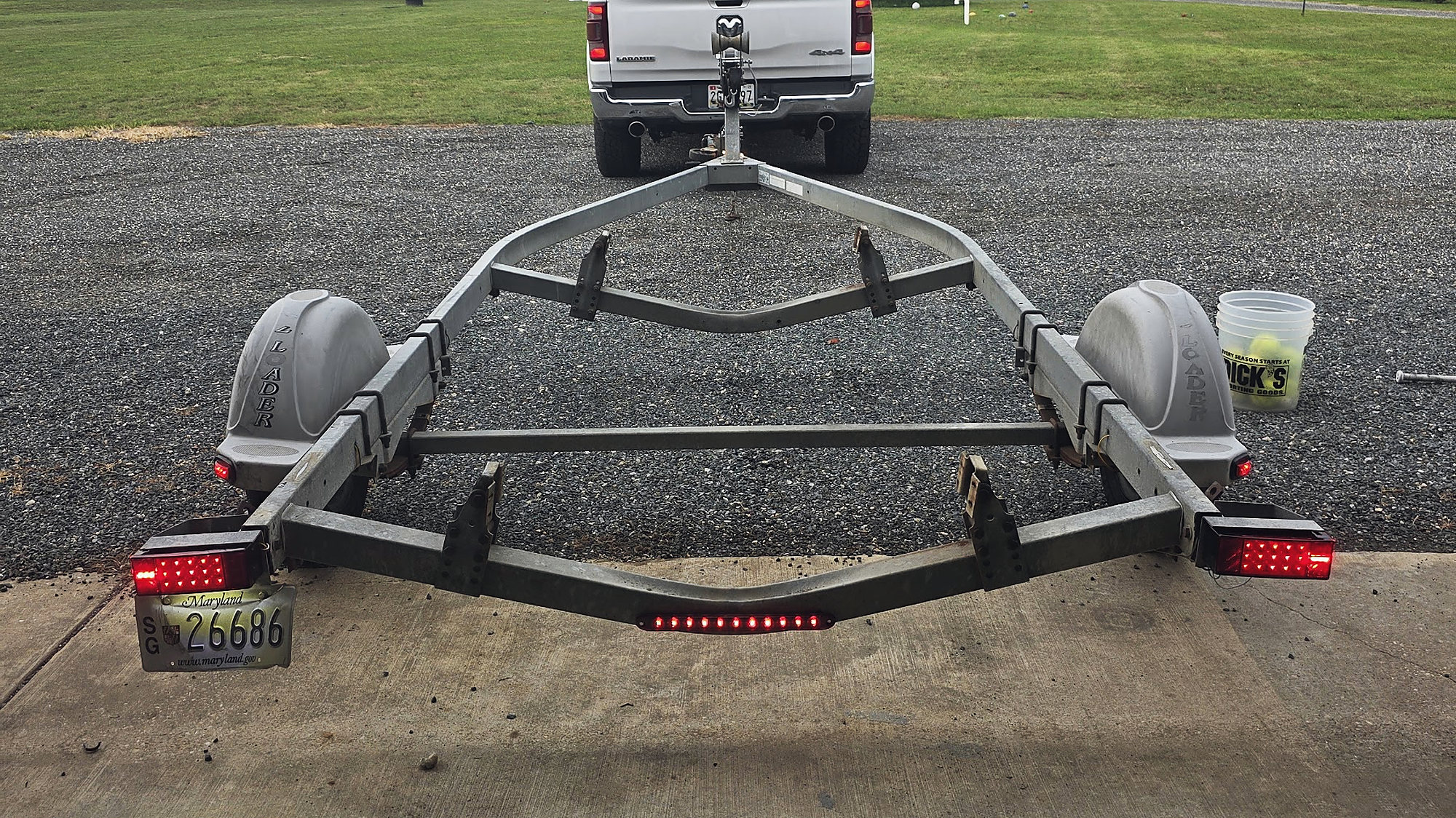 A boat trailer and truck on the gravel lot at the shop