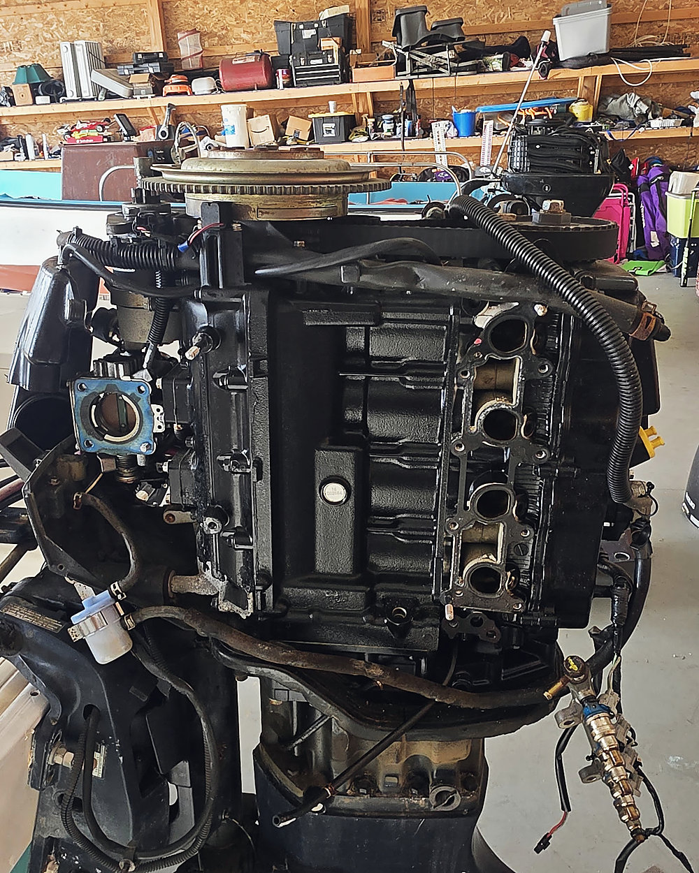 An outboard powerhead stripped down on the stand in the shop, a Suzuki cowl on the floor