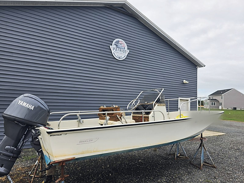 The repowered Whaler on stands outside the shop, a Yamaha outboard on the transom and the Patriot Marine sign on the wall